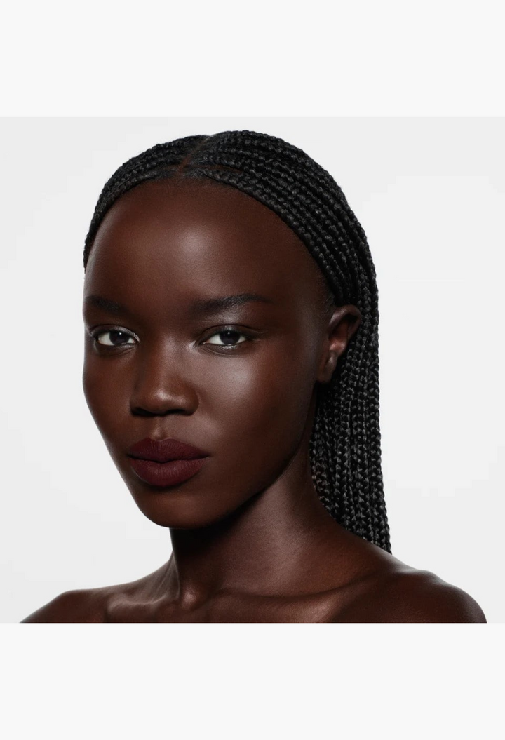 GLAM MODA Rouge Victoria matte lipstick in a deep red shade on a model with braided hair against a white background.