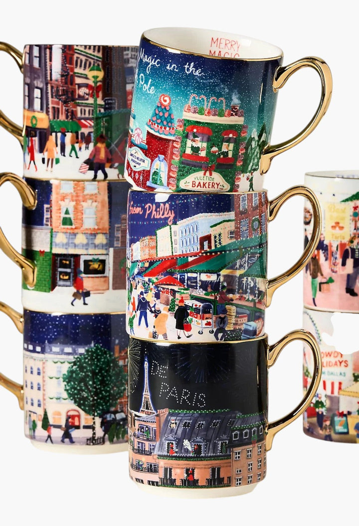 GLAM MODA Holiday in the City stoneware mugs stacked, featuring festive streetscapes and hand-painted gold handles.