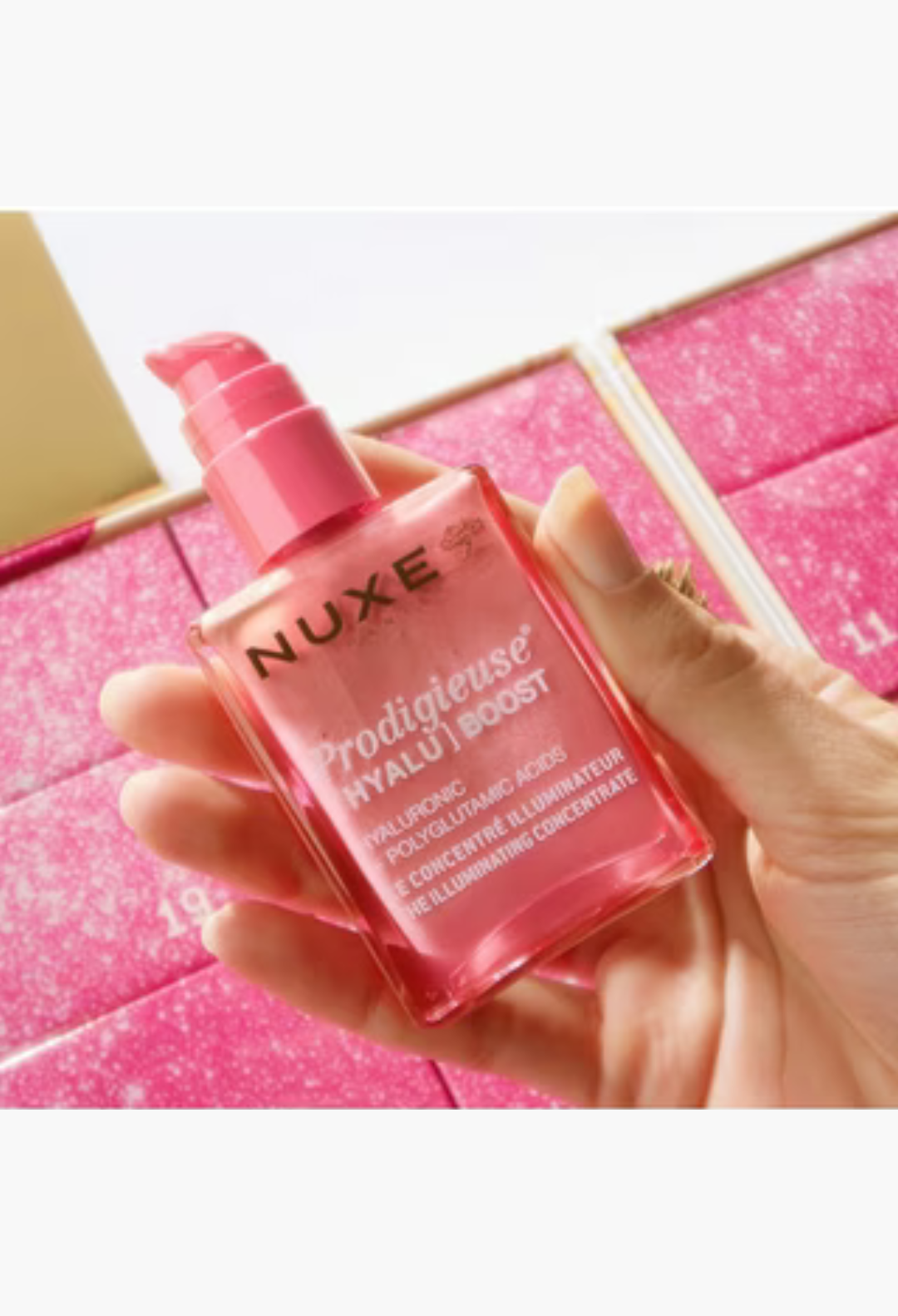 GLAM MODA Nuxe Prodigieuse Hyalu Boost illuminating concentrate held in hand against a pink advent calendar background