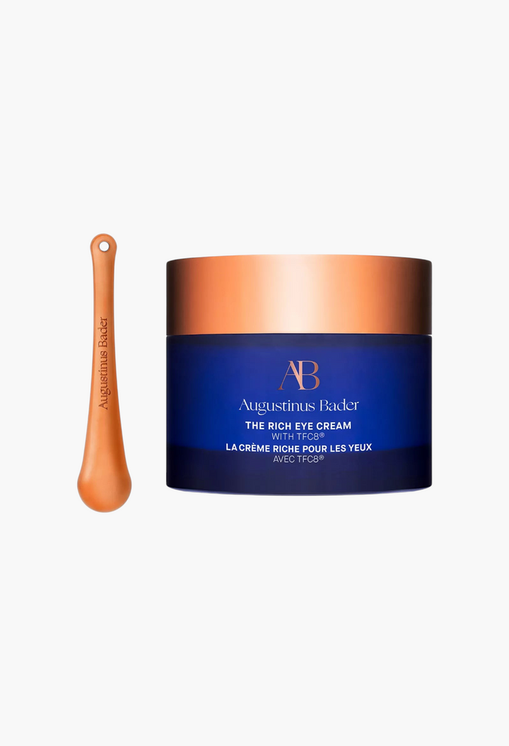 GLAM MODA Augustinus Bader The Rich Eye Cream in a blue jar with a copper lid and a matching cooling massage tool.