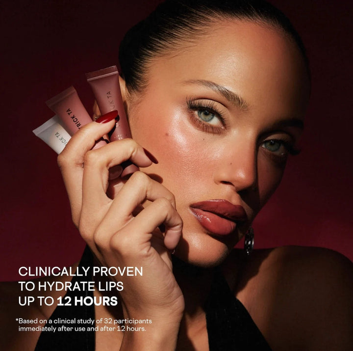GLAM MODA model holding three PATRICK TA tinted lip balm tubes against a dark red background