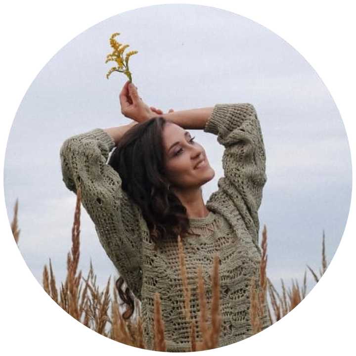 Woman in a knitted sweater holding a plant in a field
