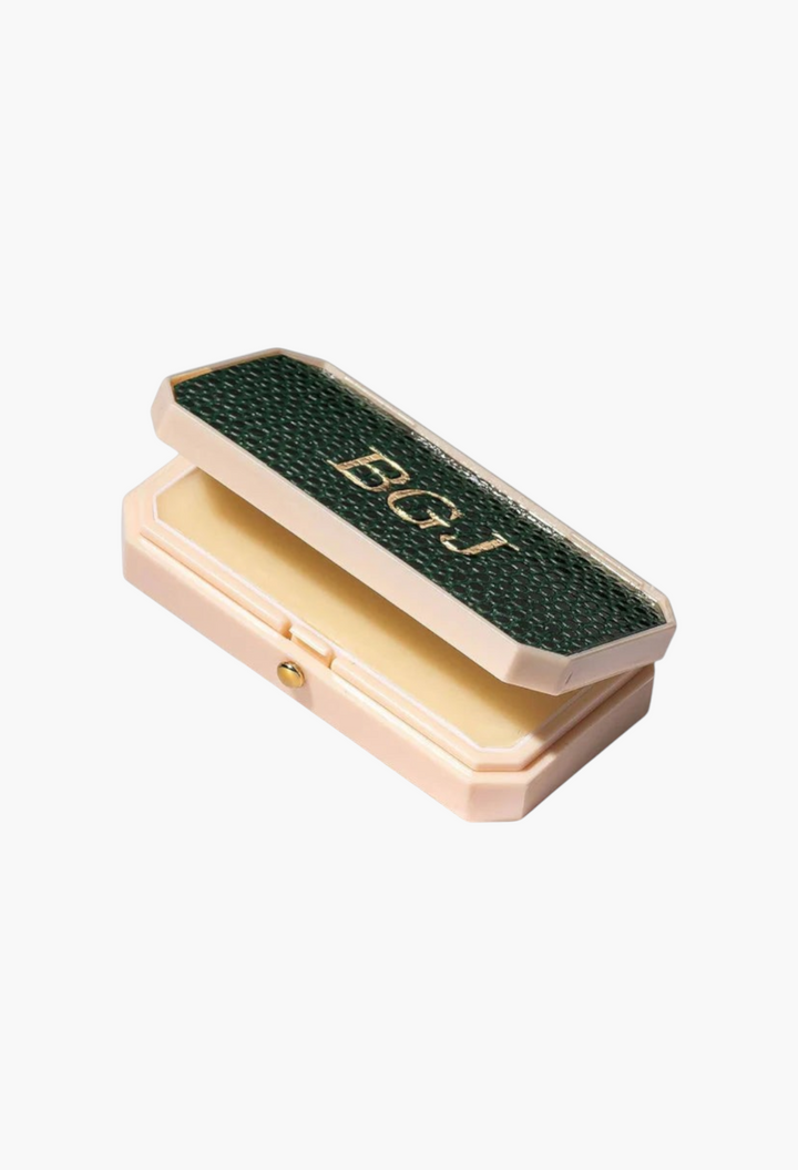 GLAM MODA Baume des Muses Ivory lip balm in a customizable green leather-like case with gold embossed initials.