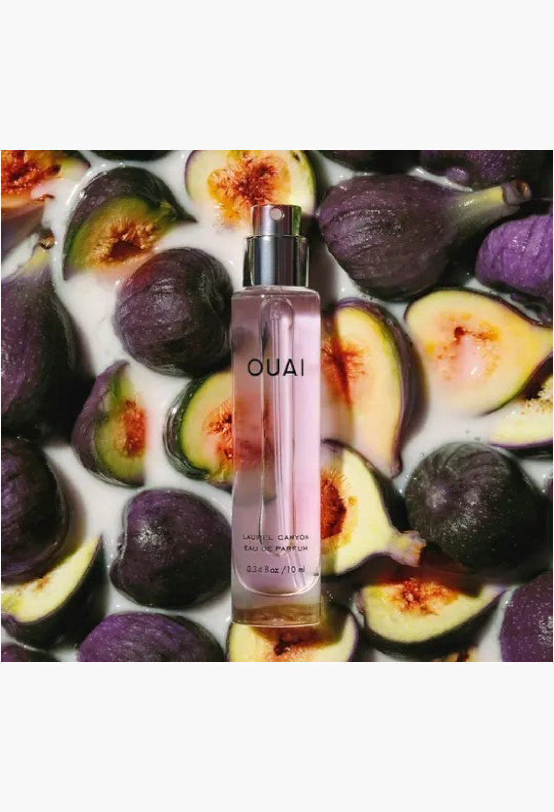GLAM MODA travel-sized OUAI Laurel Canyon Eau de Parfum bottle surrounded by fresh sliced figs in a milky liquid.