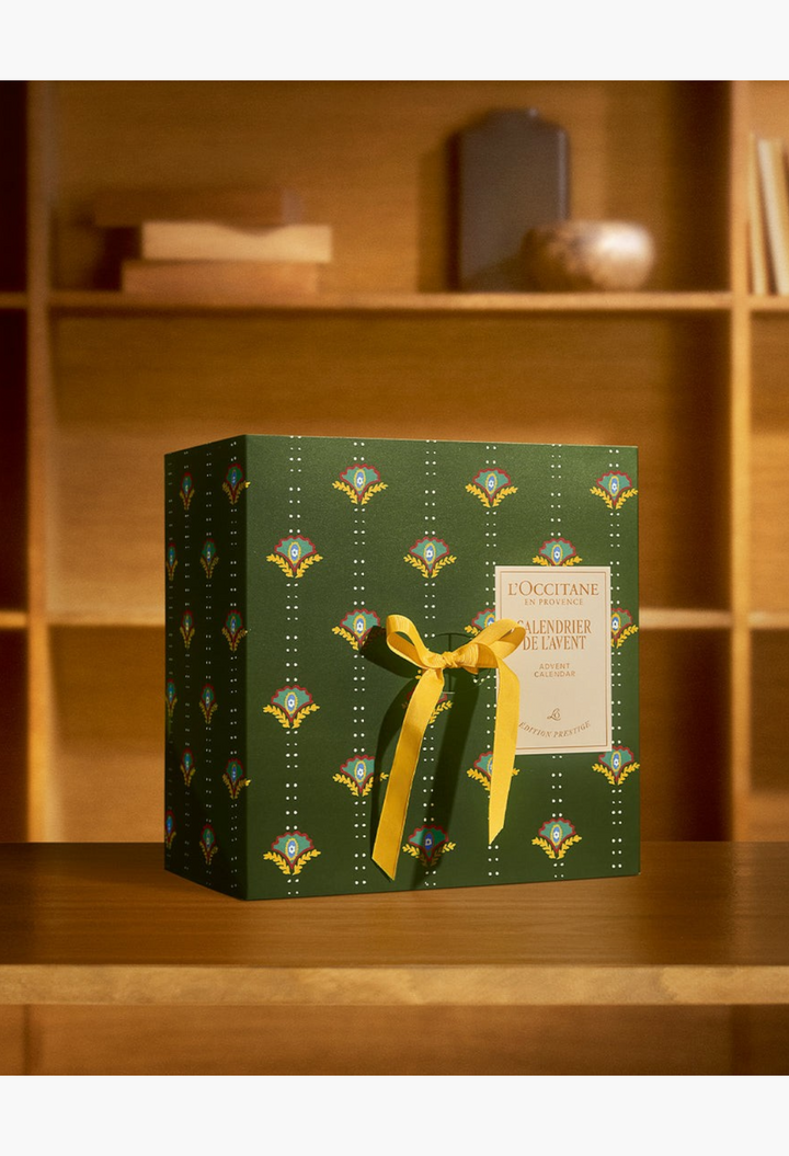 GLAM MODA Prestige Advent Calendar in a green box with floral patterns and a yellow ribbon on a wooden table.