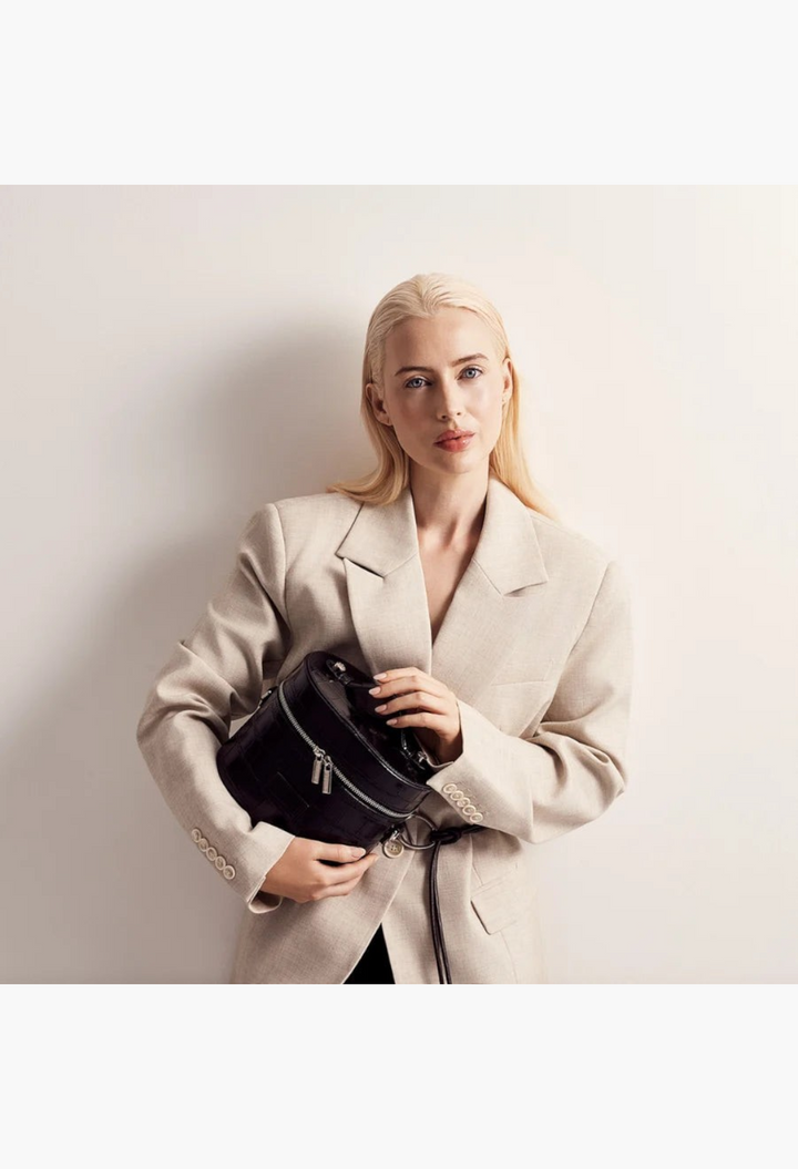 GLAM MODA oval black vegan leather toiletry case held by a blonde model wearing a beige blazer