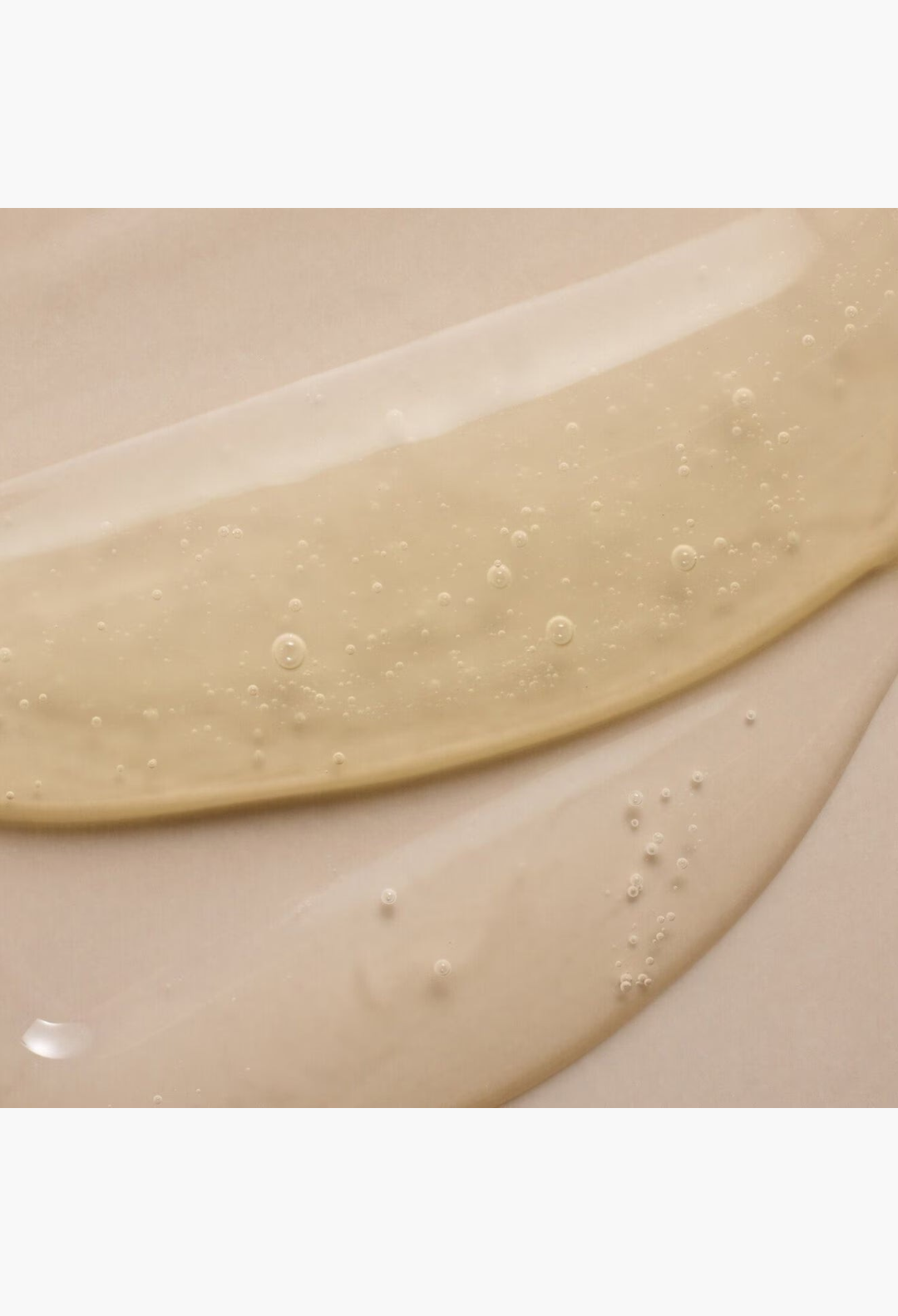 GLAM MODA GRO revitalizing shampoo texture showing a clear, golden-hued gel formula with small air bubbles.
