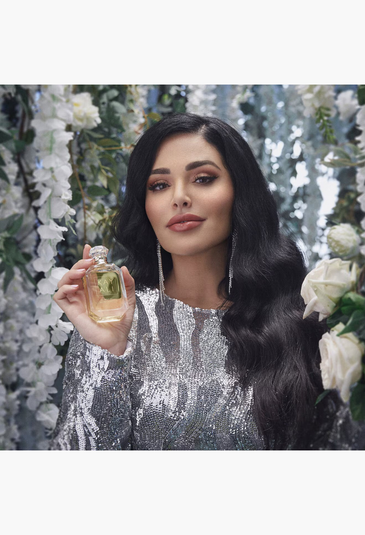 GLAM MODA model holding a glass bottle of Kayali Déjà Vu White Flower | 57 perfume with a silver sequined dress