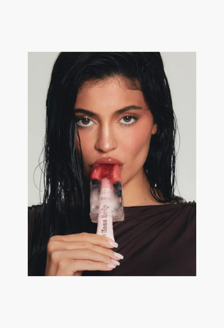 GLAM MODA Kylie by Kylie Jenner Gloss Drip lipgloss on model with wet hair holding a fruit popsicle