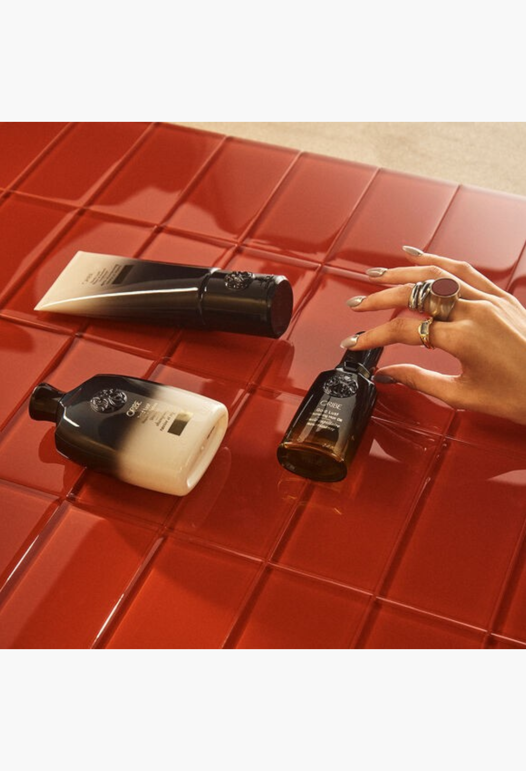 GLAM MODA Oribe Gold Lust haircare set featuring shampoo, conditioner, and nourishing oil on a glossy red tiled surface.