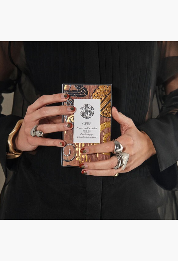 GLAM MODA Oribe Protect and Texturize Travel Duo set held in hands, featuring heat protection and texturizing sprays.