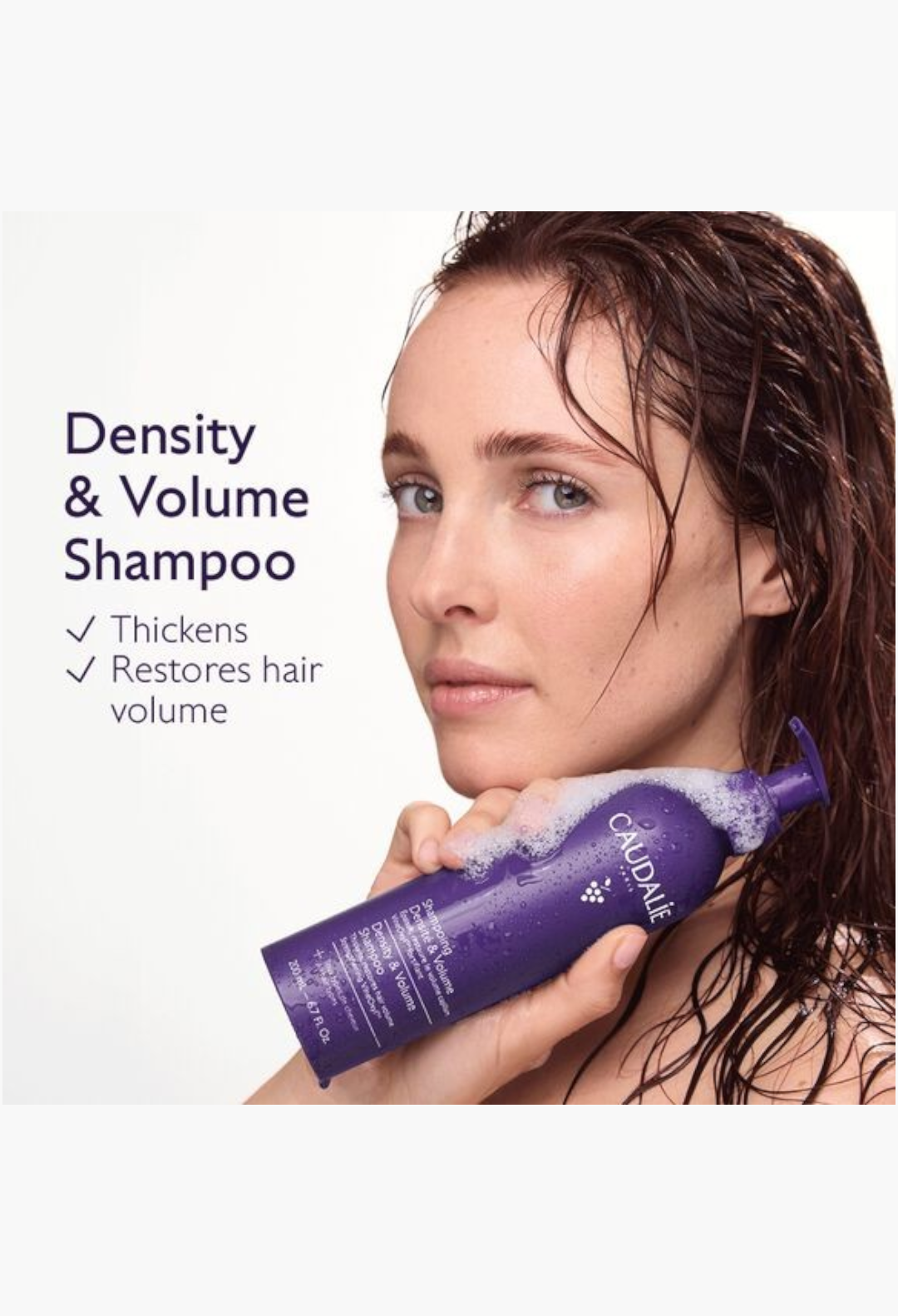 GLAM MODA Caudalie Density and Volume Shampoo bottle held by a woman with wet hair to promote thicker, fuller hair.