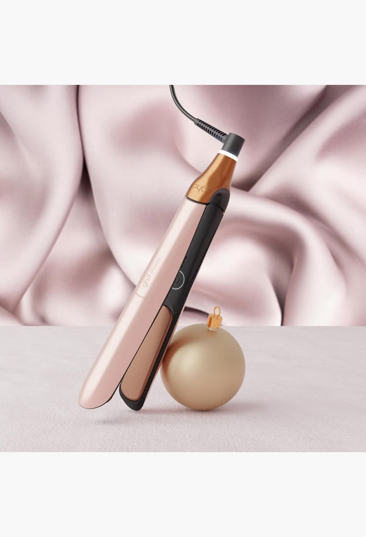 GLAM MODA ghd Chronos hair straightener in metallic rose gold with a matching Christmas ornament on a white background