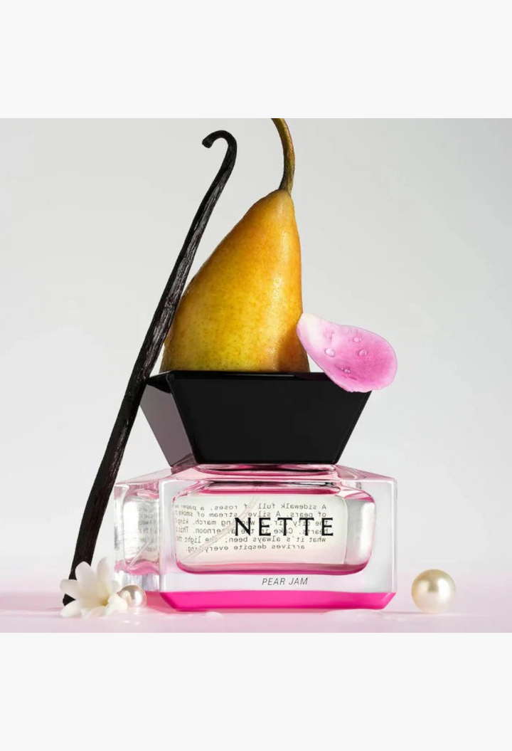 GLAM MODA Nette Pear Jam perfume bottle with a fresh pear, vanilla bean, and flower petal on a white background.