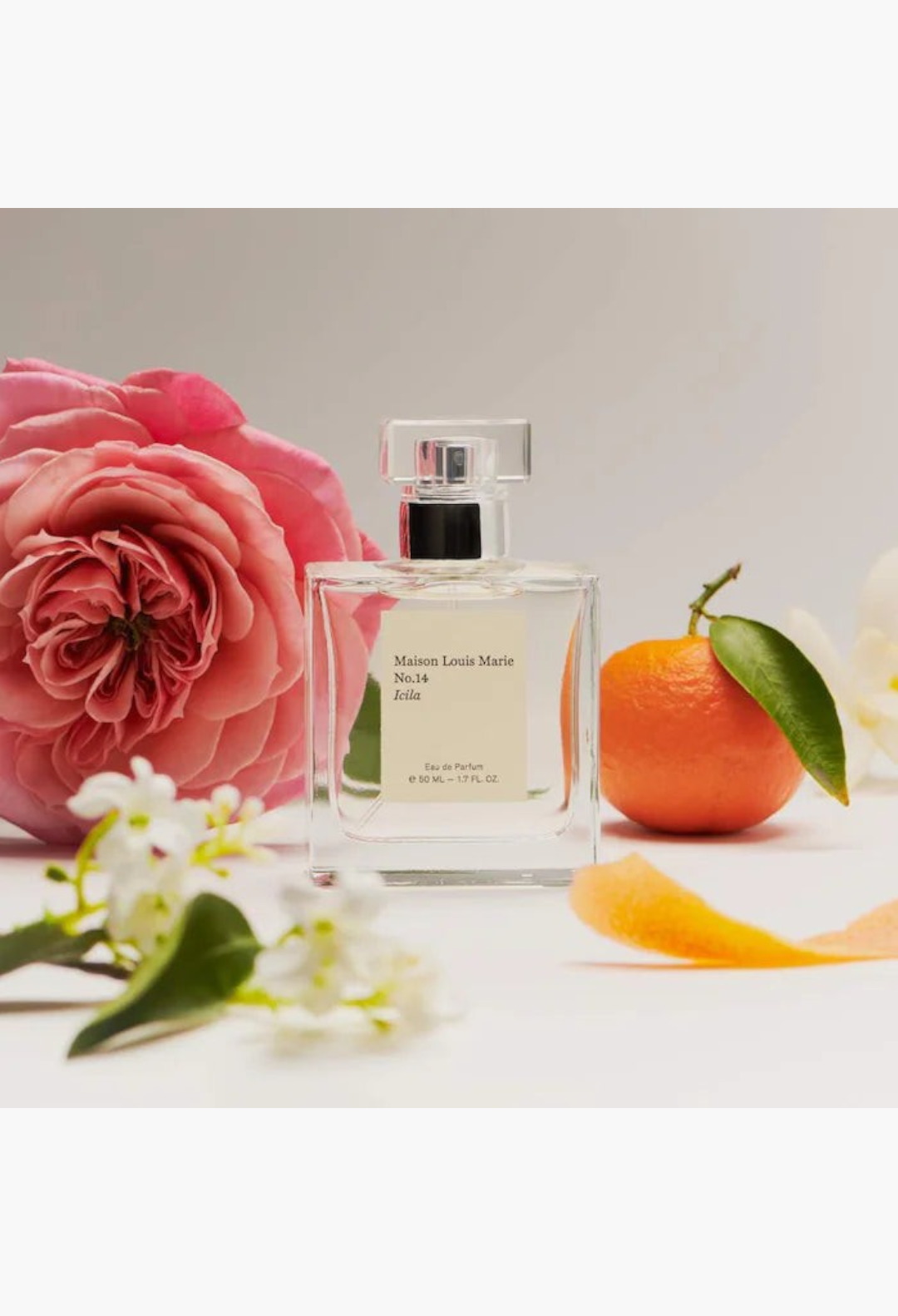 GLAM MODA Maison Louis Marie No.14 Icila perfume bottle surrounded by a pink rose, a fresh orange, and white flowers.