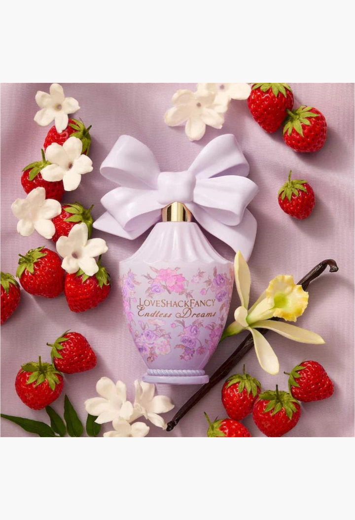 GLAM MODA LoveShackFancy Endless Dreams perfume bottle with a lavender bow, surrounded by strawberries and flowers.