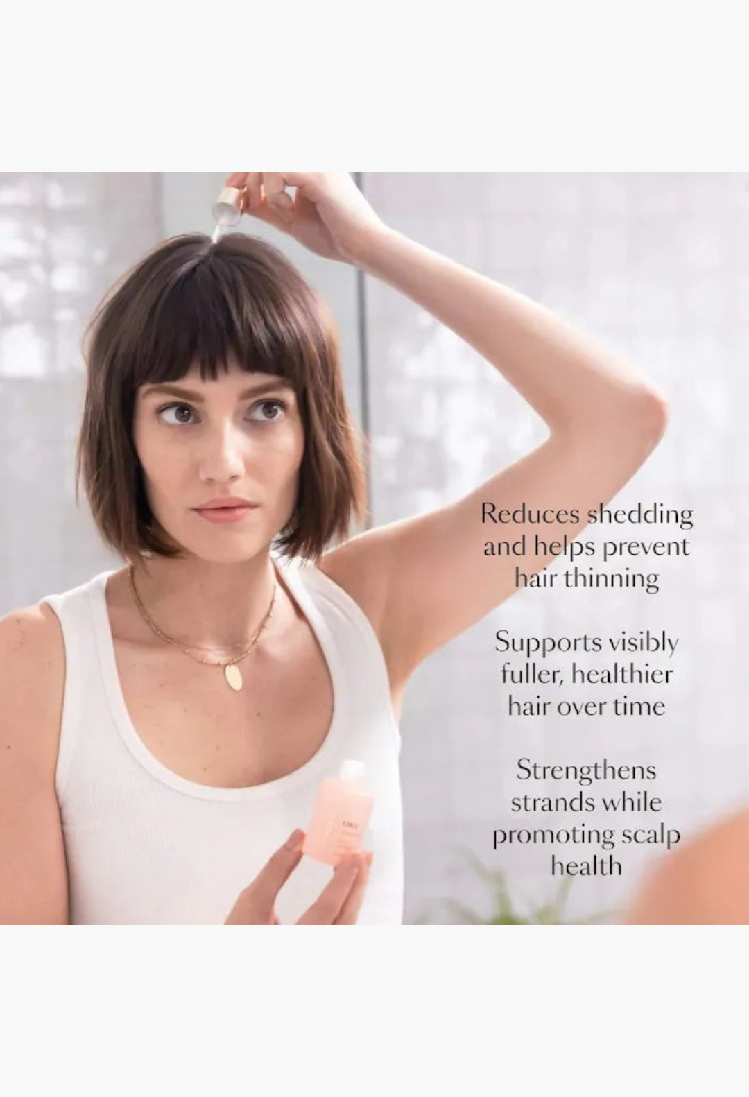 GLAM MODA model applying hair serum from a small bottle to her dark bob hairstyle against a white background
