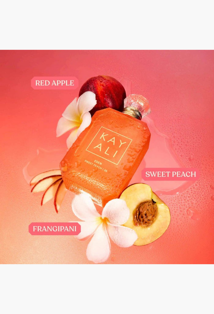 GLAM MODA Kayali Eden Sweet Peach perfume bottle surrounded by fresh peach slices and tropical flowers