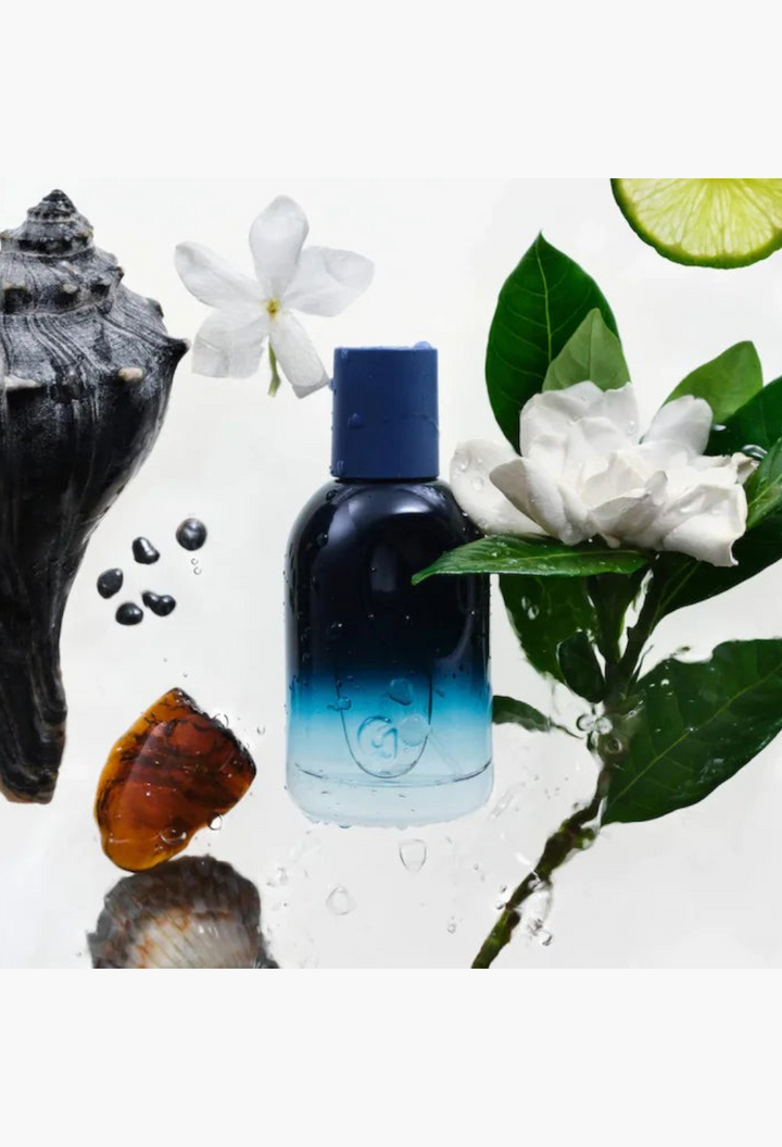 GLAM MODA Golden Hour perfume bottle with blue ombre glass, surrounded by white flowers, seashells, and lime slices.