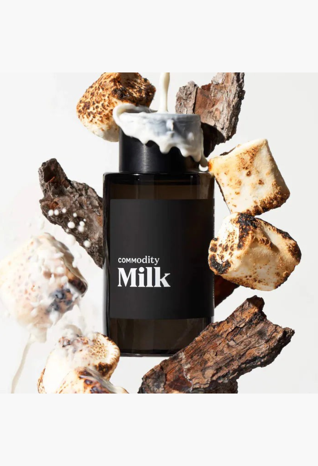 GLAM MODA Commodity Milk perfume bottle surrounded by toasted marshmallows and wood bark with milk pouring over top