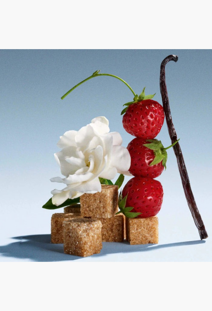 GLAM MODA perfume sampler set ingredients featuring fresh strawberries, a white gardenia flower, brown sugar cubes, and a vanilla bean.